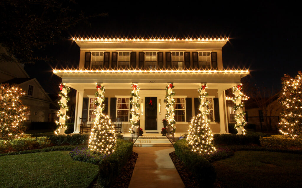 Warm white Christmas lights along the roofline and entry trees of a two-story Orlando home