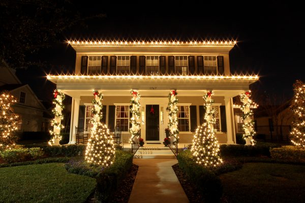 Warm white Christmas lights along the roofline and entry trees of a two-story Orlando home